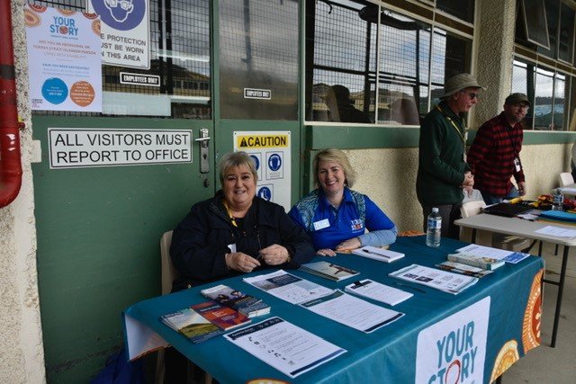 Two smiling women with short blonde hair sit behind a table with brochures at a prison