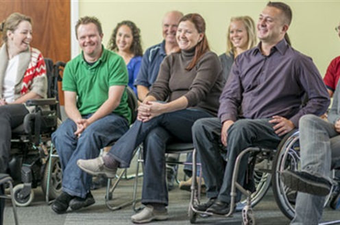 A group of smiling people sit in a support group meeting